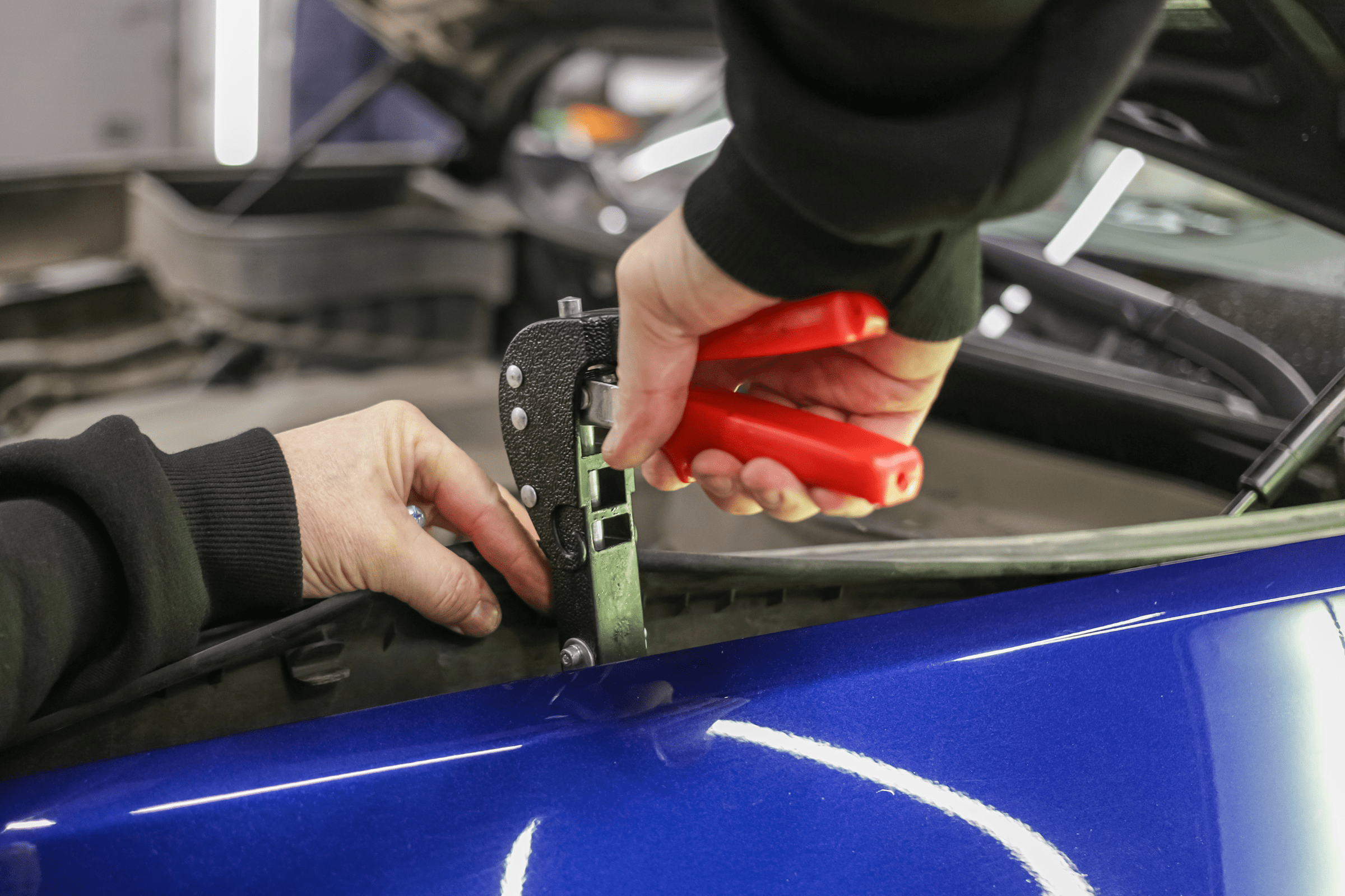 Person using pliers on blue car.