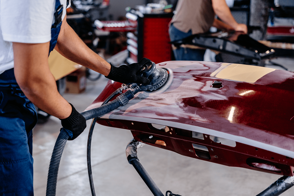 Worker sanding a car hood in workshop.