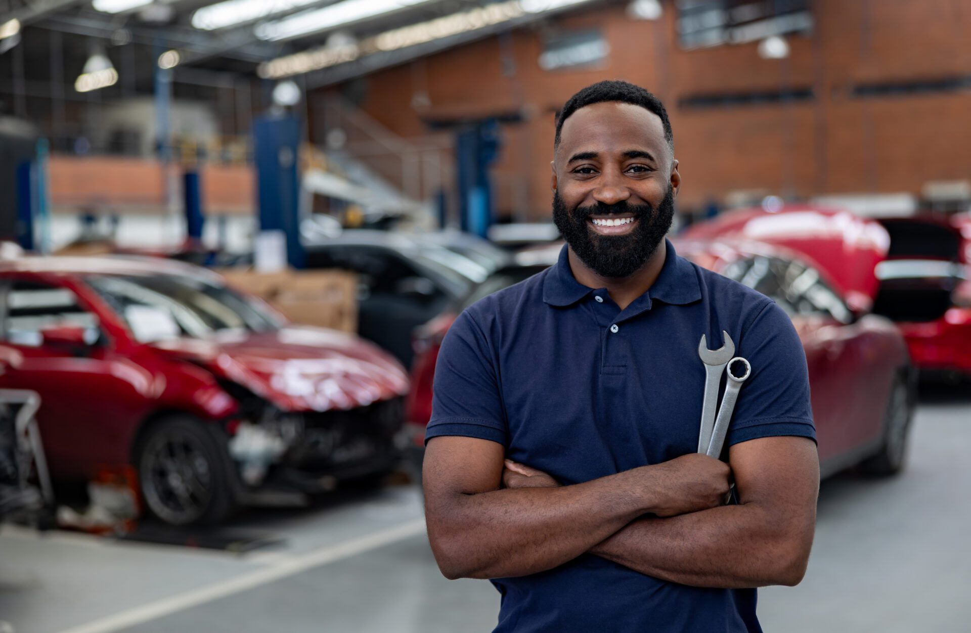 Smiling mechanic holding wrench in auto shop.