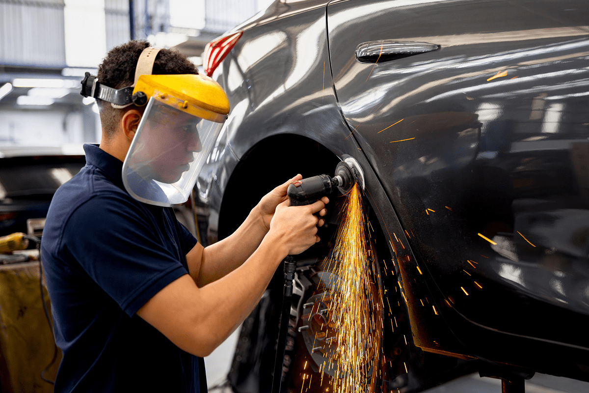 Worker grinding car with sparks flying.